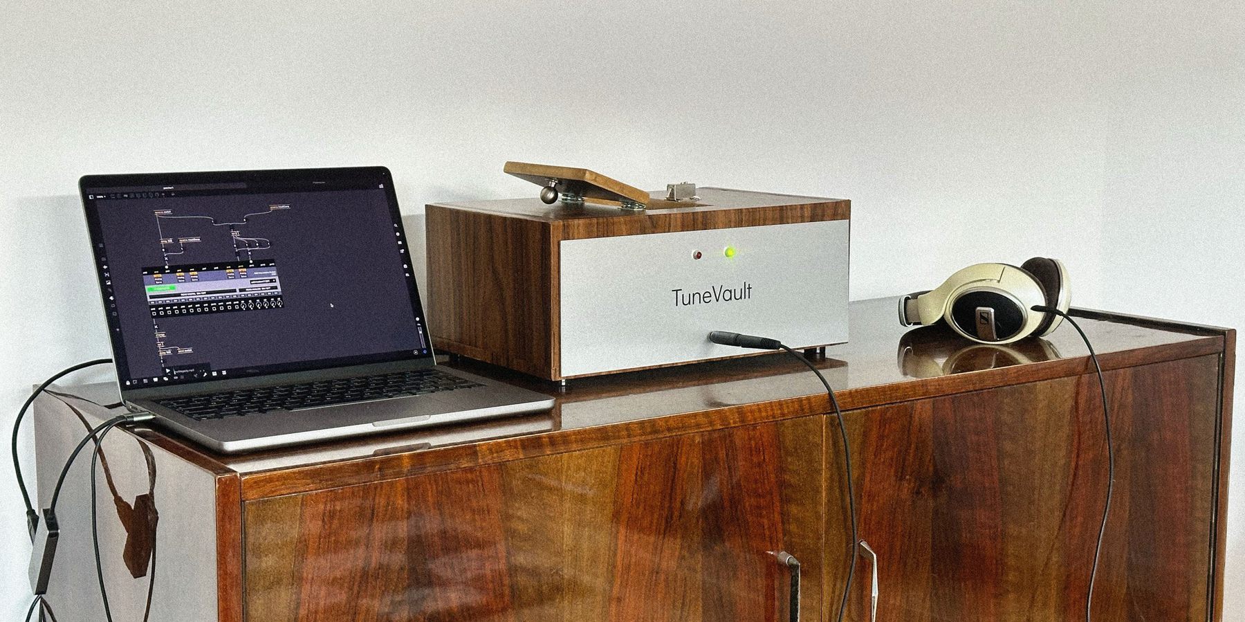 TuneVault with its hatch open on a wooden sideboard, next to a laptop and a pair of headphones, ready to be used