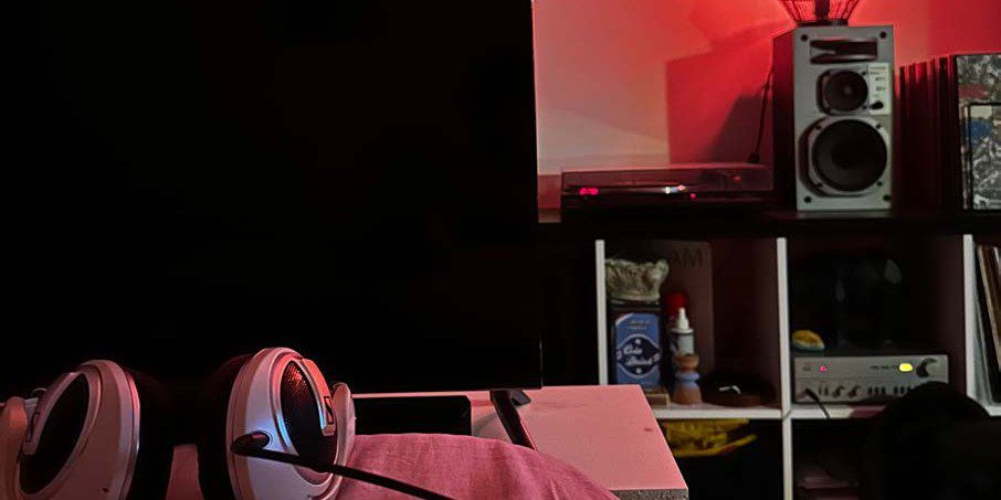 Headphones on a cushion in a dark room, with a record collection and speakers in the background