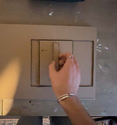 A hand sliding the cardboard hatch shut over the phone