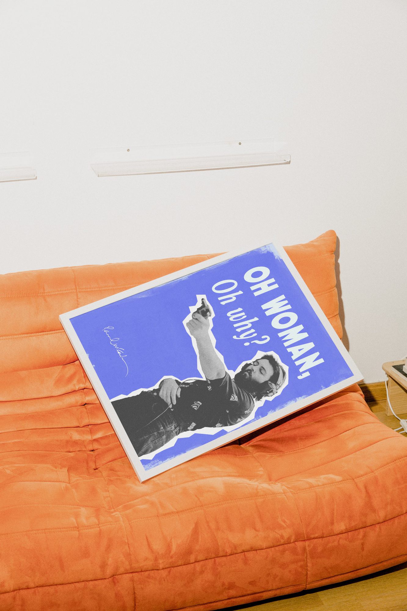The Paul McCartney poster in a white frame, lying on an orange sofa
