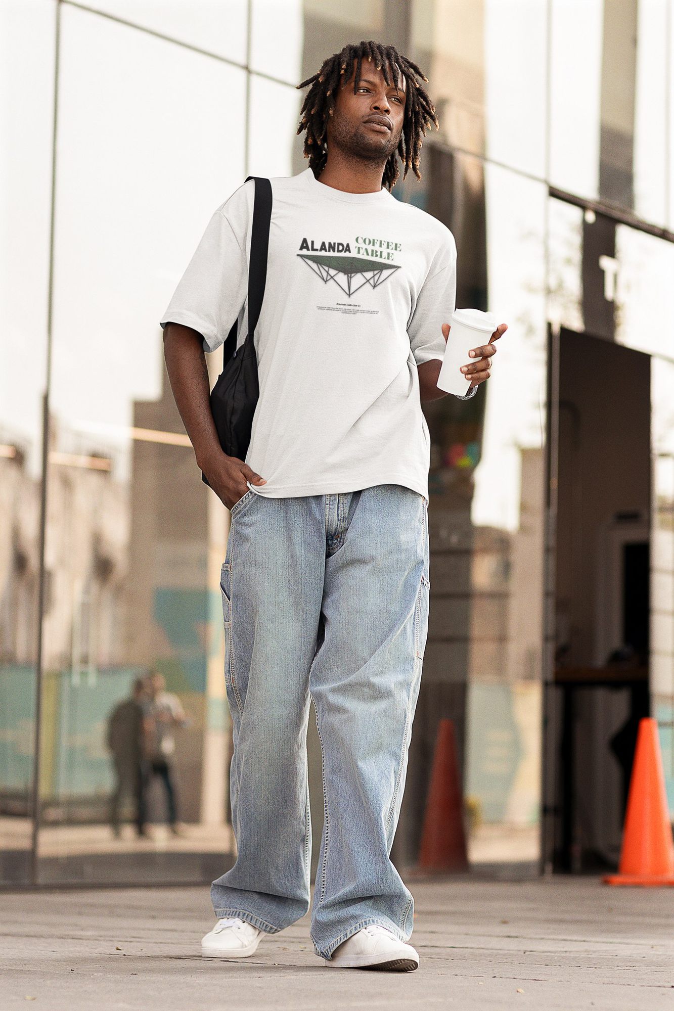 Model wearing the Alanda Coffee Table tee from the Bateman Collection, walking past a glass building